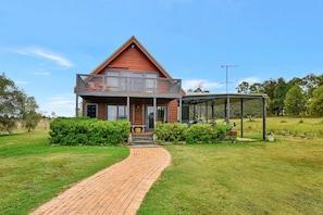 A two-story house with a balcony, a covered outdoor area, and a brick pathway leading to the entrance.