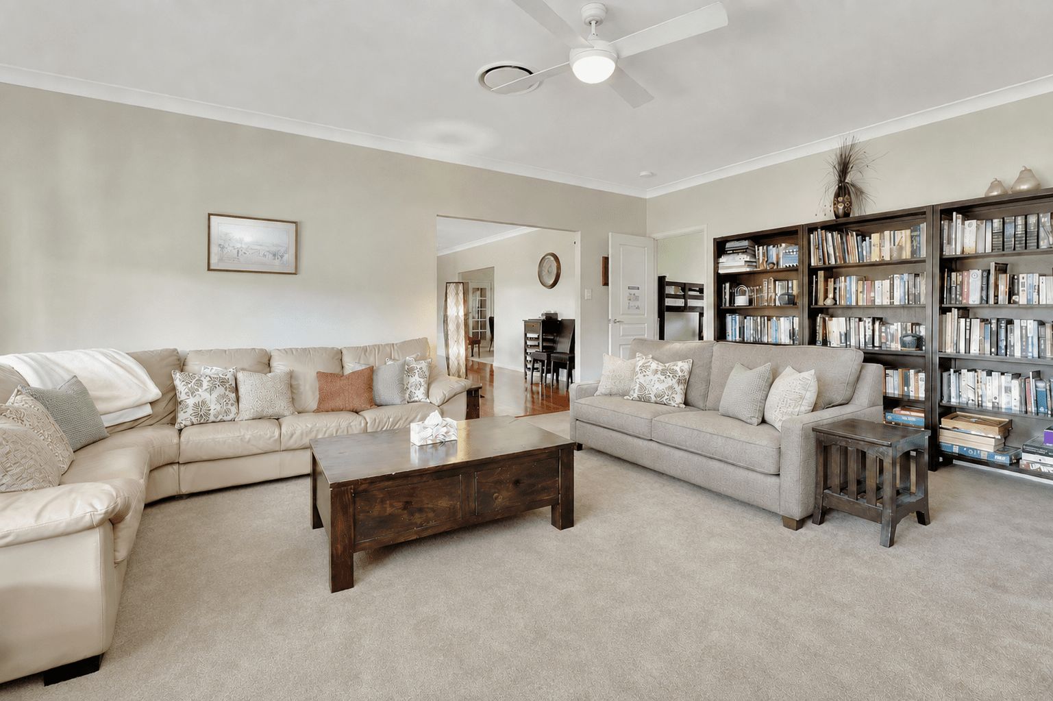 A living room with two sofas, a coffee table, a bookshelf, and a ceiling fan.