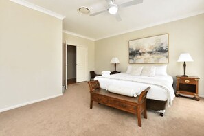 A bedroom with a bed, bedside tables, a chair, a ceiling fan, and a door leading to another room. - Olive Ridge Homestead - Set across 43 peaceful acres in the heart of Pokolbin (Rothbury)