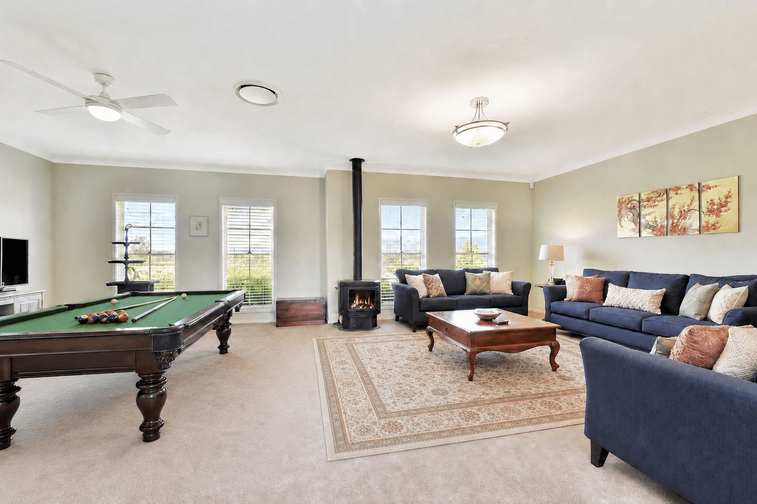 A living room with a pool table, sofas, a fireplace, and large windows.