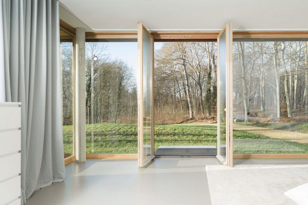 A room with large windows, a white floor, and a view of a forest.