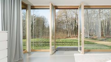 A room with large windows, a white floor, and a view of a forest.