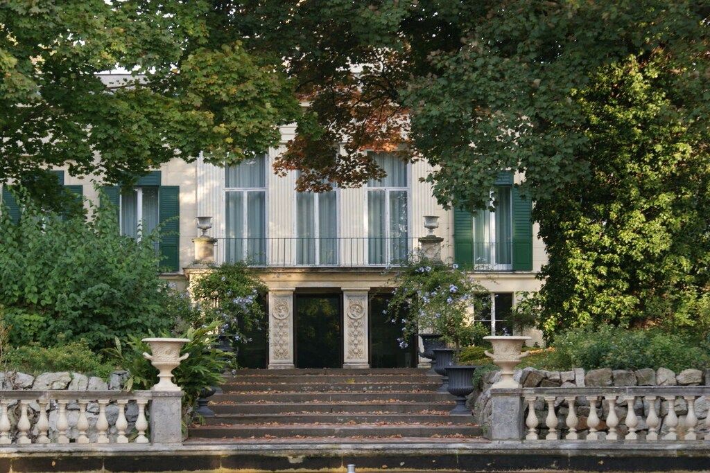 A classical building with a symmetrical facade, a central entrance with steps, and a balustrade.