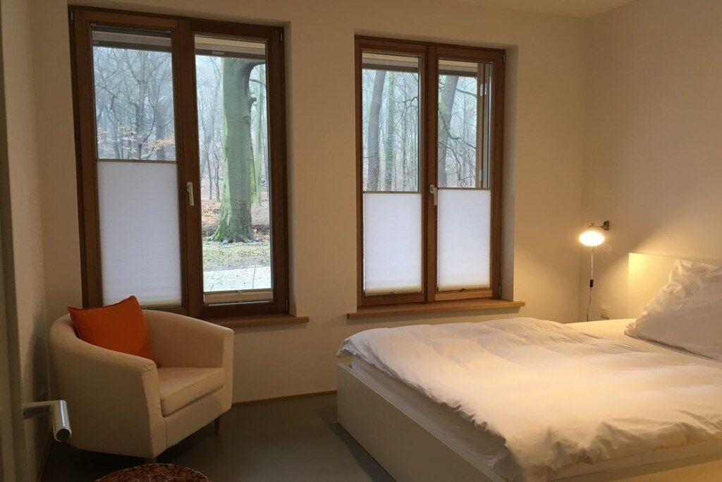 A bedroom with a bed, a chair, and two windows.