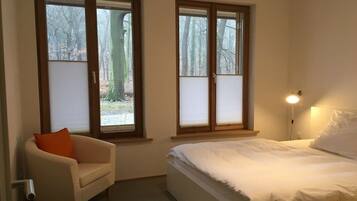 A bedroom with a bed, a chair, and two windows.