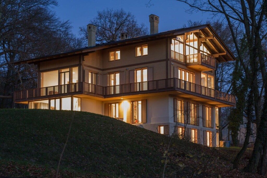 A multi-story house with balconies and large windows, surrounded by trees.