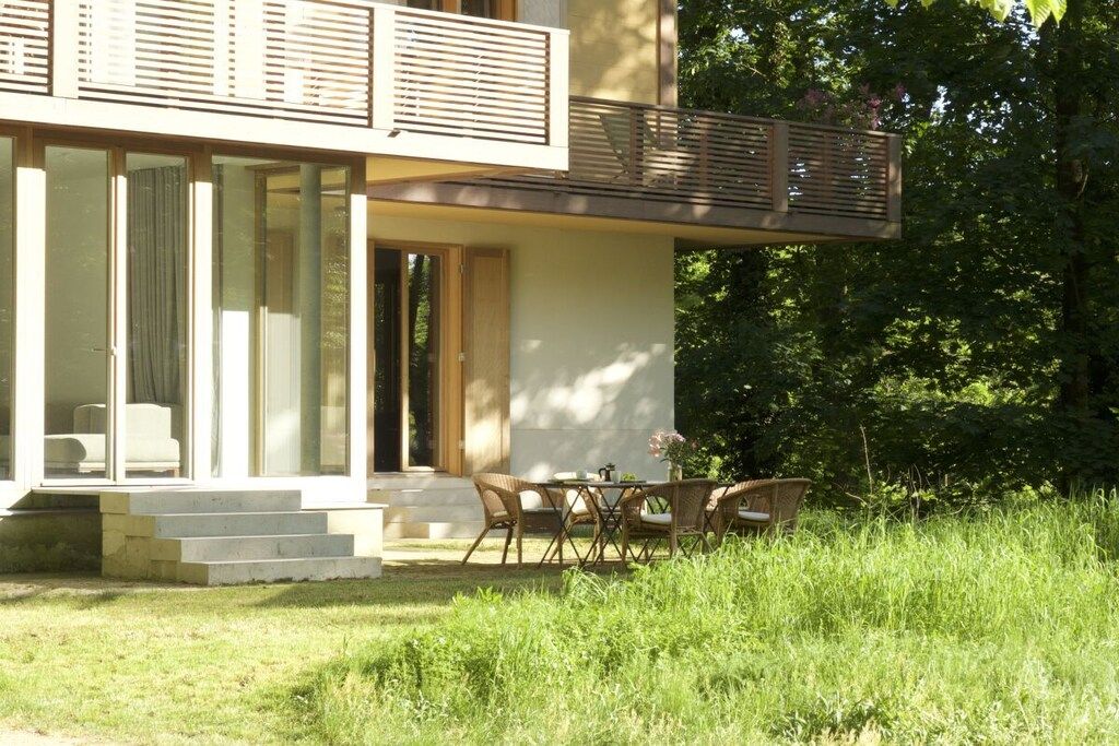 Et moderne hus med balkon, spiseområde med fletmøbler og en have.