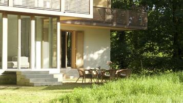 Et moderne hus med balkon, spiseområde med fletmøbler og en have.