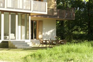 Et moderne hus med balkon, spiseområde med fletmøbler og en have.