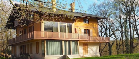 A two-story house with a balcony, large windows, and a grassy yard.