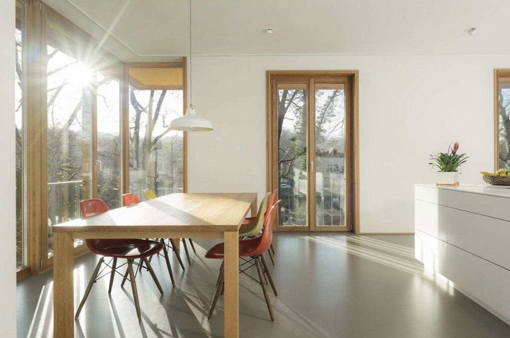 A modern dining area with a wooden table and chairs, large windows, and a view of the outdoors.