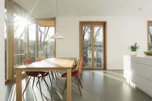 Et moderne spiseområde med et træbord og stole, store vinduer og udsigt til naturen.