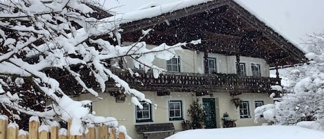 A traditional chalet with a sloped roof, wooden balcony, and a snow-covered entrance.