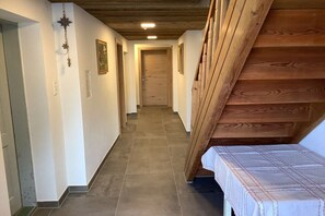 Un corridoio con una scala in legno sulla destra, una porta in fondo e un letto con copripiumino bianco a sinistra.
