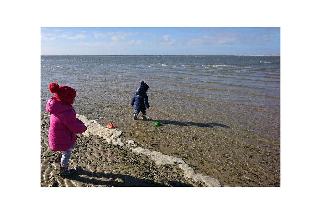 Dos niños jugando cerca del agua bajo un cielo despejado.