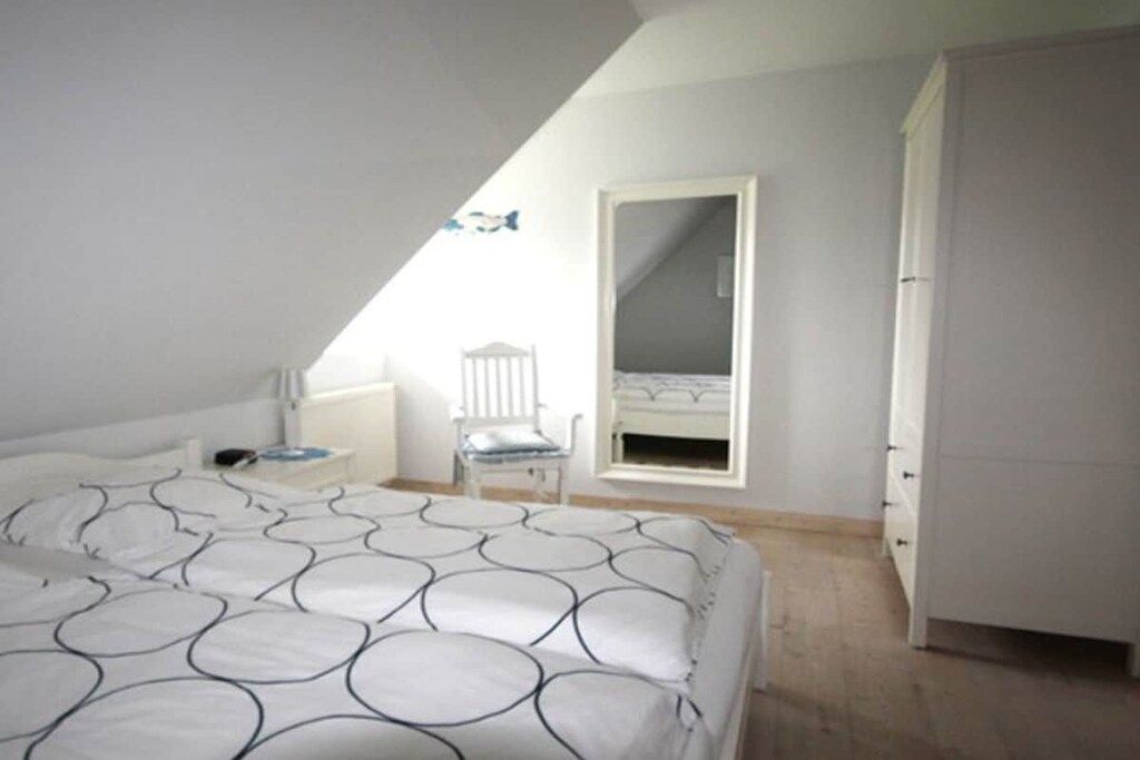 A bedroom with a bed, a chair, a wardrobe, and a window.