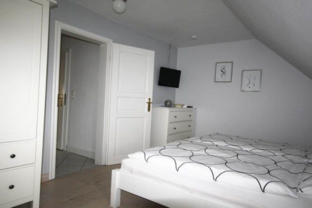 A bedroom with a bed, a dresser, a television on the wall, and a door leading to another room.