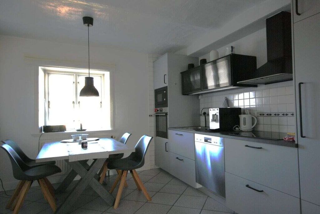A modern kitchen with white cabinets, a dining table with chairs, a window, and a hanging light fixture.