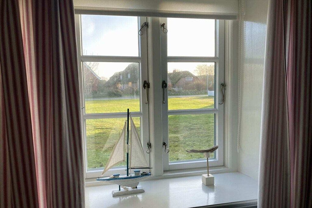 Ein Zimmer mit einem großen Fenster, Vorhängen und einem Modellsegelboot auf dem Fensterbrett.