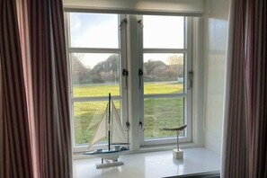 Een kamer met een groot raam, gordijnen en een model zeilboot op de vensterbank.