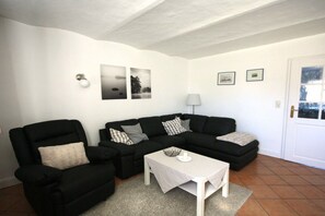 A living room with a black sofa set, a white coffee table, and a lamp. There are framed pictures on the wall. - Holiday apartment with 2 bedrooms (Utersum auf Föhr)