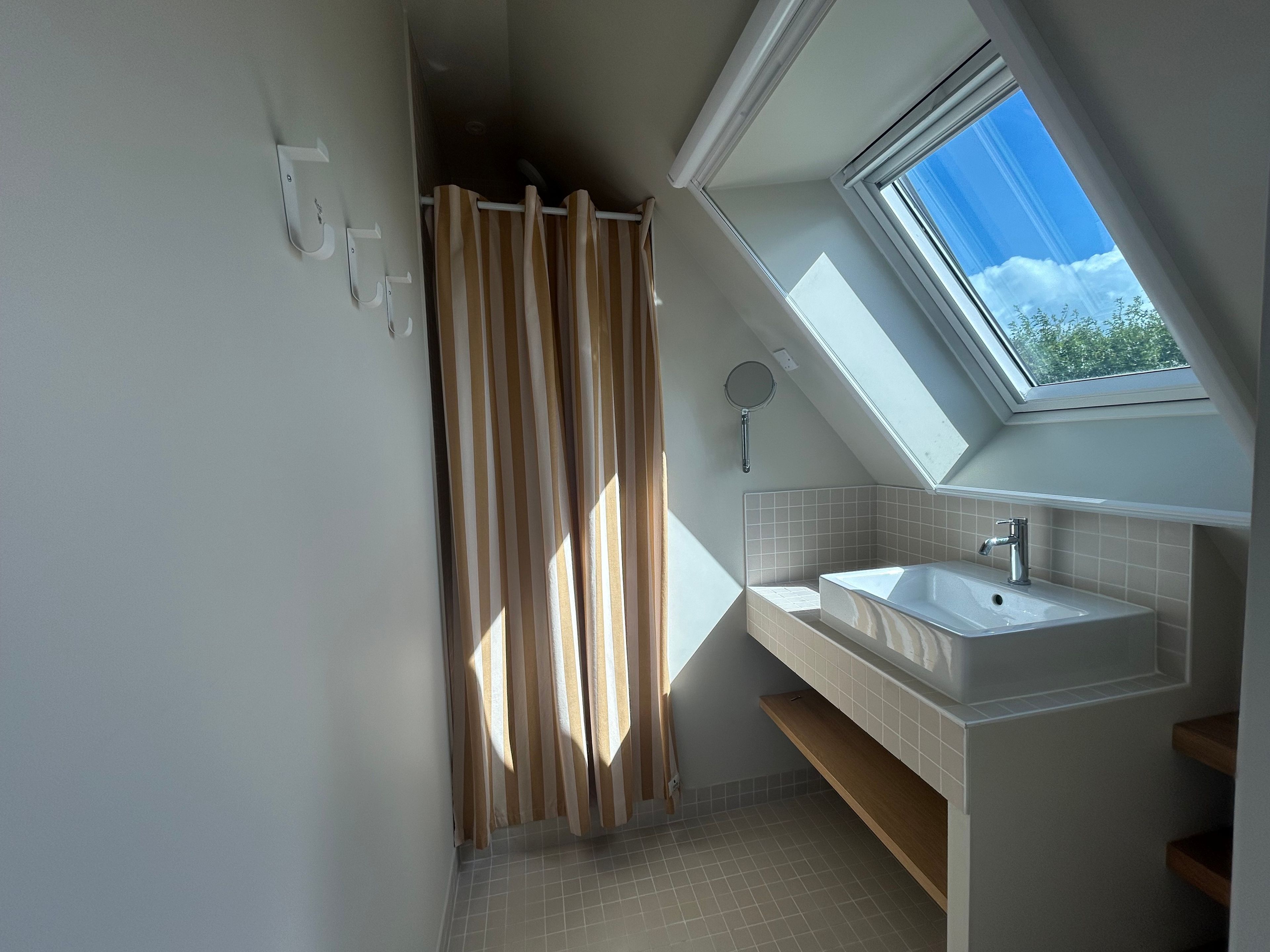 Une salle de bain moderne avec un puits de lumière, un rideau de douche et un lavabo.