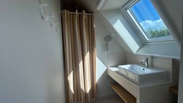 Une salle de bain moderne avec un puits de lumière, un rideau de douche et un lavabo.
