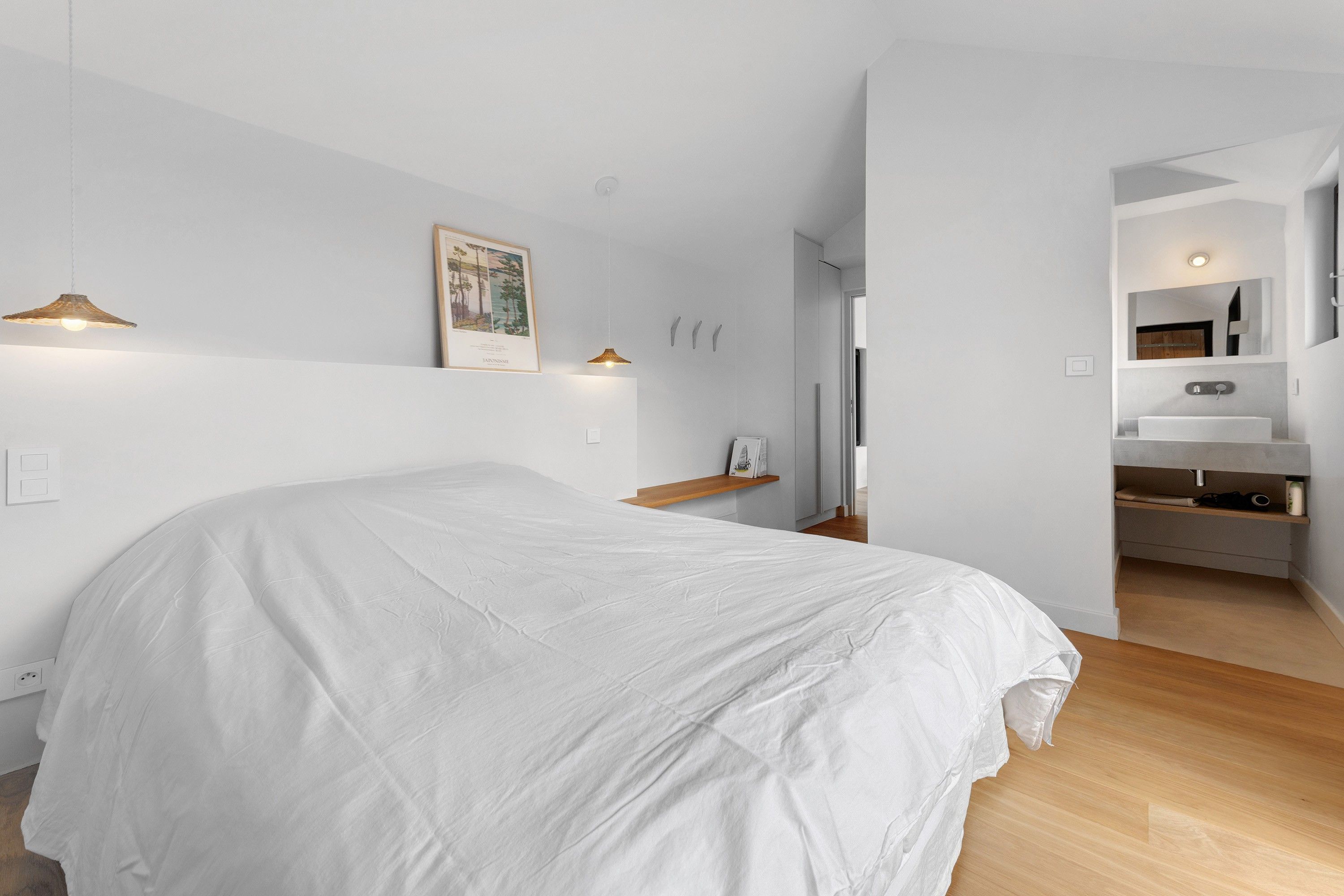 A bedroom with a bed, bedside lamps, a framed picture, and a walk-in closet with a mirror and a sink.
