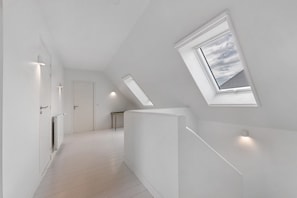 Un couloir moderne et minimaliste, doté d’un plafond en pente et de lucarnes.