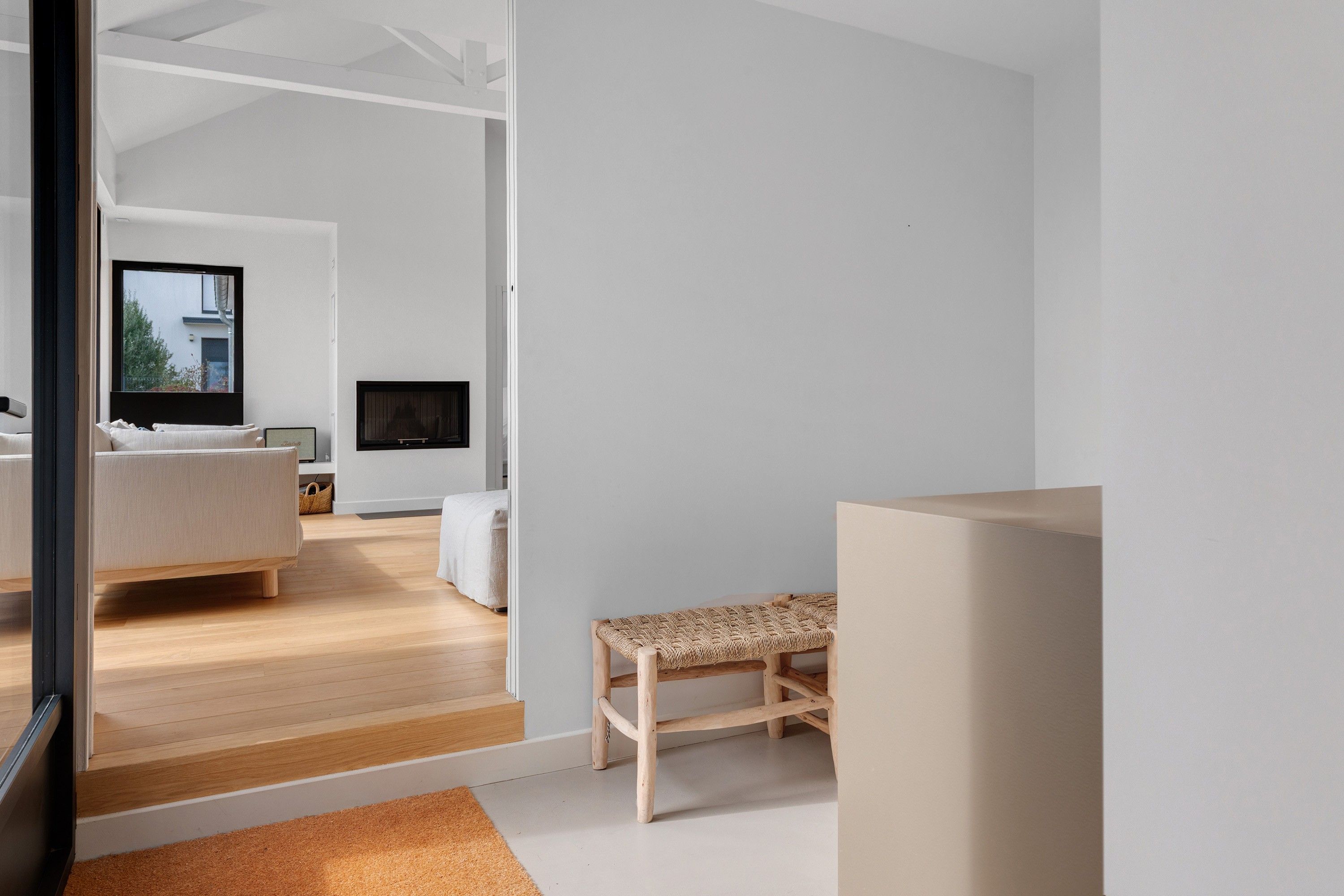 A modern, minimalist living space with a large window, a sofa, a television, and a wooden bench.