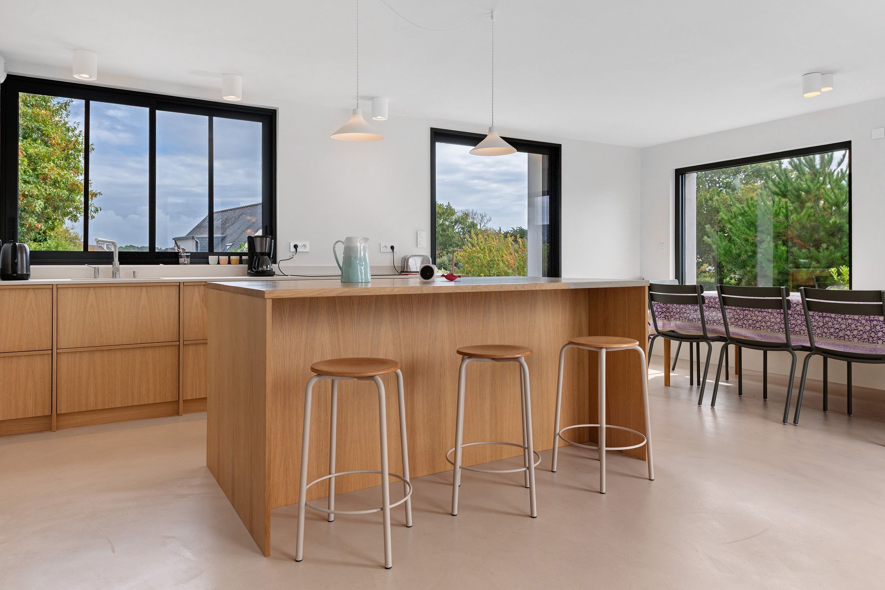 A modern kitchen with a large island, bar stools, and a dining area with chairs.