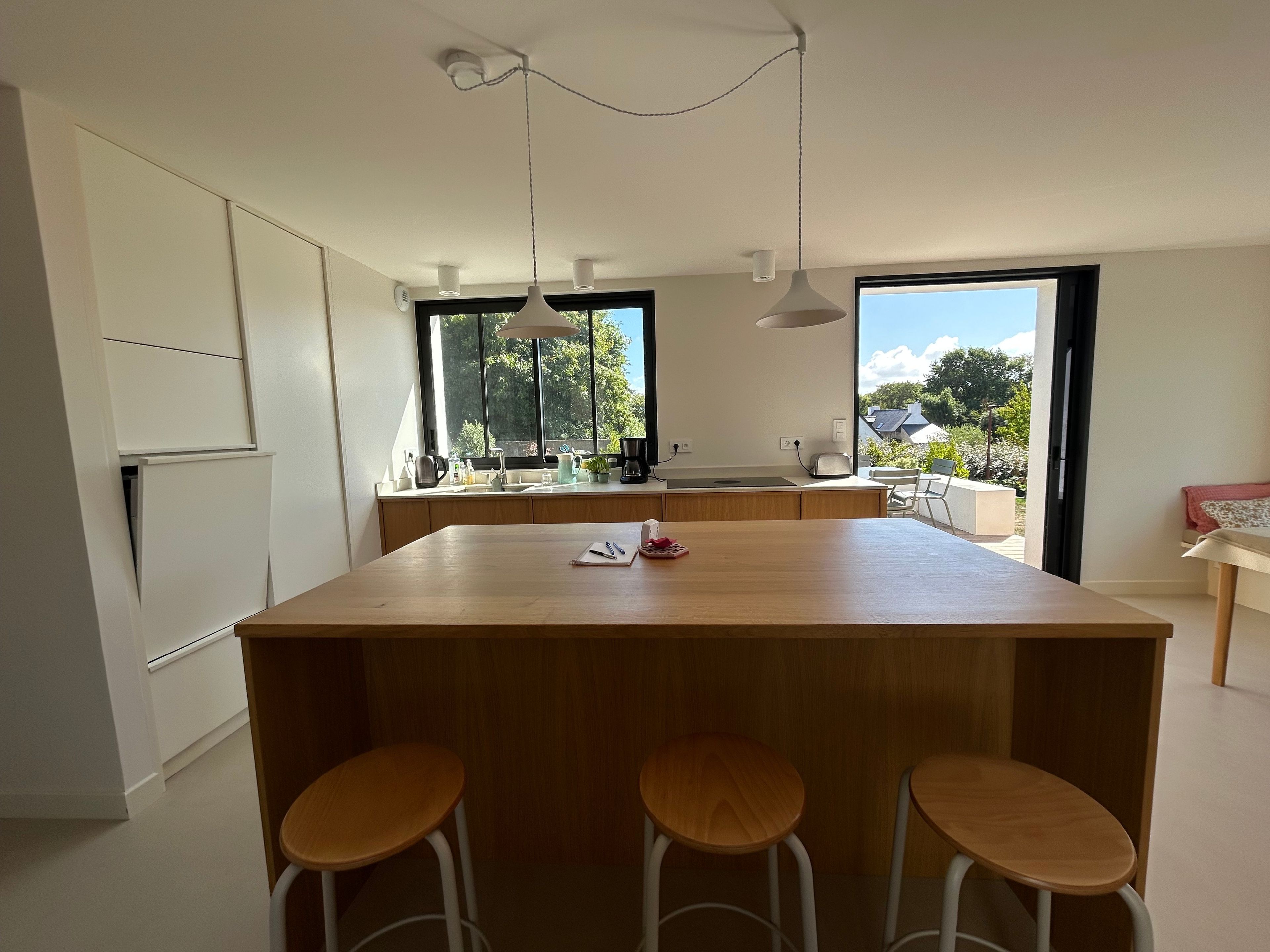 Une cuisine moderne dotée d’un îlot central, de tabourets de bar et de grandes fenêtres.