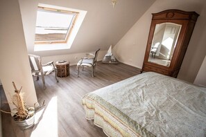 A bedroom with a sloped ceiling, a large bed, a wooden wardrobe, a chair, a small table, and a potted plant. - Holiday apartment with 3 bedrooms (Breege\/ Juliusruh OT Breege)