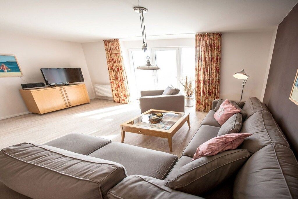Una sala de estar con un sofá, una mesa de centro, un televisor sobre un mueble bajo y cortinas.