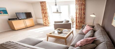 Una sala de estar con un sofá, una mesa de centro, un televisor sobre un mueble bajo y cortinas.