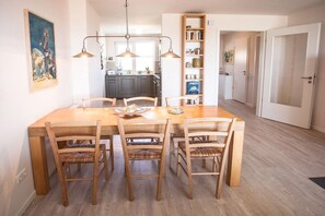 Un coin repas avec une table et des chaises en bois, un luminaire suspendu et une bibliothèque.