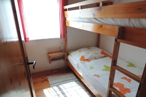 Ein Schlafraum mit Etagenbett, einer Holztür, einem kleinen Nachttisch und einem Fenster mit roten Vorhängen.