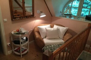 A cozy room with a curved sofa, a small table with a cup and apple, a lamp, and a window with a sailboat decoration. - Holiday apartment with 2 bedrooms (Schönwalde a.B.)