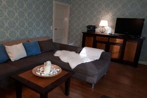 Ein Wohnzimmer mit einer Couch, einem Couchtisch mit Dekoration, einem Fernseher auf einem Schrank und einer Wand mit Muster.