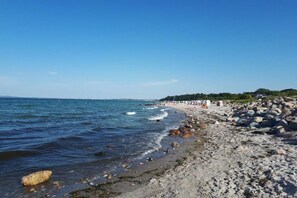 A beach with rocky shoreline, clear blue sky, and distant trees. - Holiday apartment with 2 bedrooms (Schönwalde a.B.)