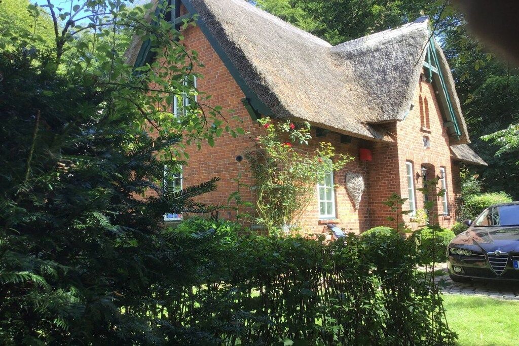 A traditional brick house with a thatched roof, surrounded by lush greenery and a parked car.