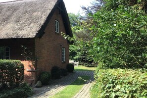 A brick house with a thatched roof, surrounded by greenery and a paved path. - Holiday apartment with 2 bedrooms (Schönwalde a.B.)