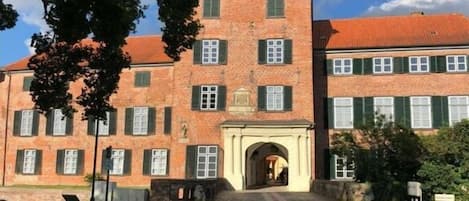 Ein historisches Gebäude mit einem zentralen Bogenportal, Backsteinfassade und grünen Fensterläden.