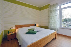 Une chambre à coucher avec un lit en bois, une table de chevet, une lampe et une fenêtre avec des rideaux.
