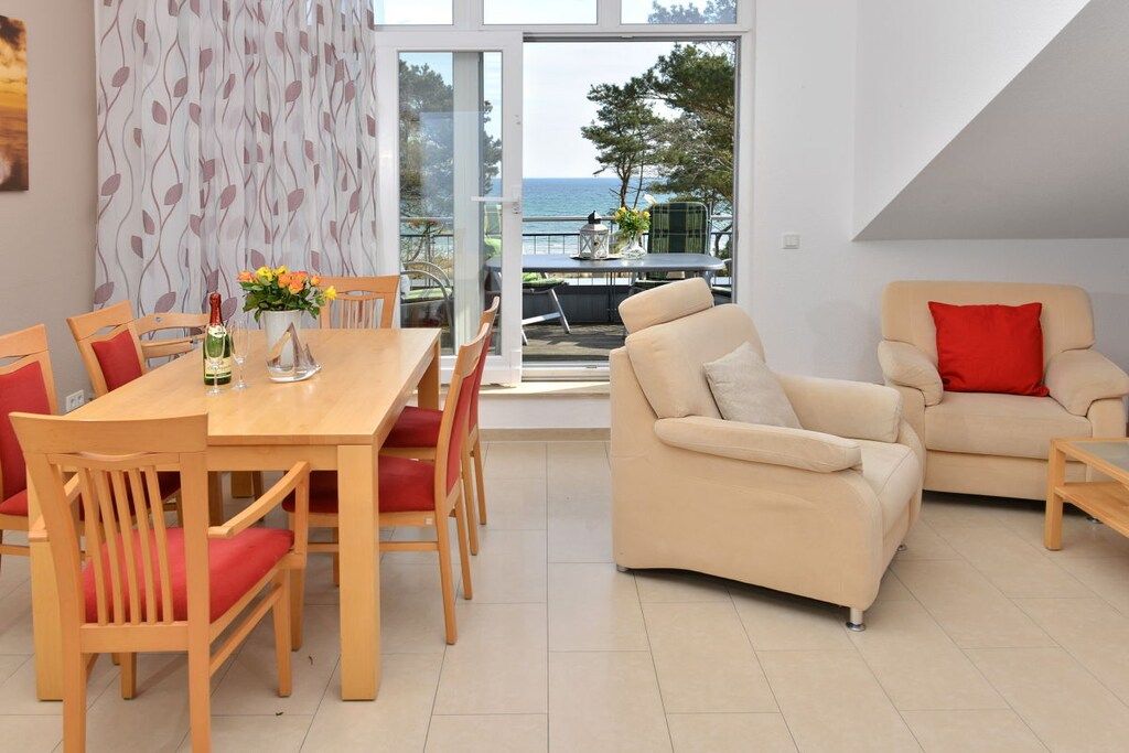 Ein modernes Wohnzimmer mit Essbereich, einer Couch und Meerblick durch große Fenster.