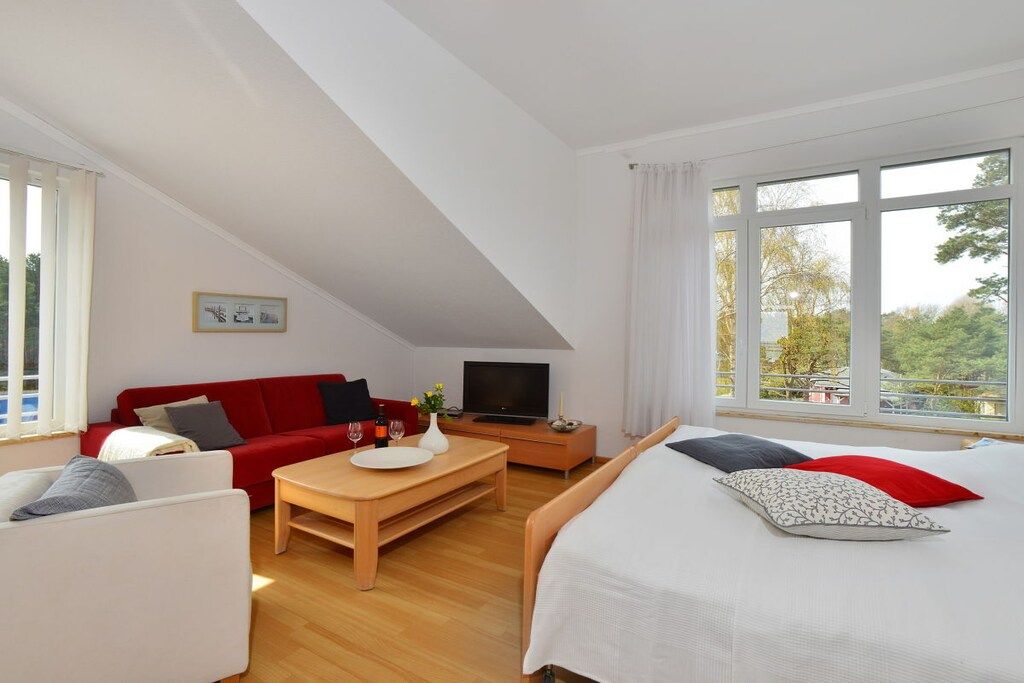 Une pièce comprenant un lit, un canapé rouge, une table en bois et un téléviseur.