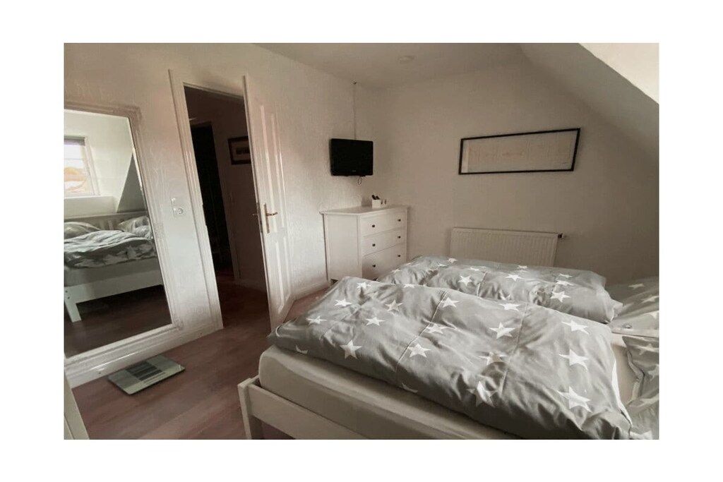 Une chambre à coucher avec un lit, une commode, un téléviseur et un radiateur.