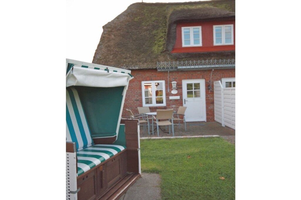 A thatched-roof house with a red brick exterior, a white door, and a small patio area with a bench and a table.