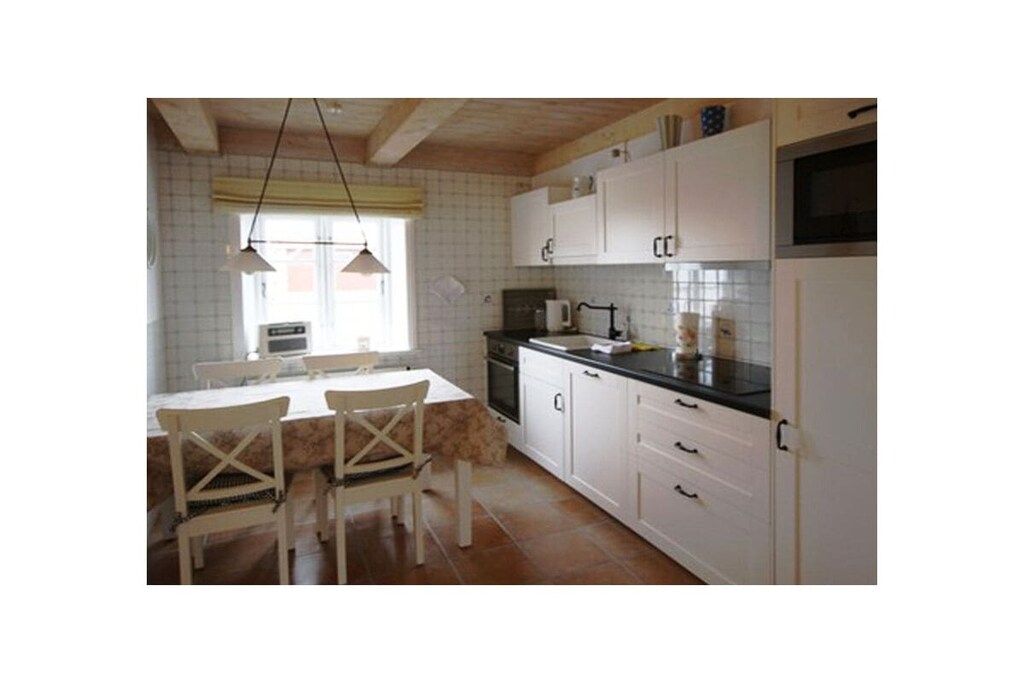 Une cuisine avec des meubles blancs, un plan de travail noir et une table à manger avec des chaises.