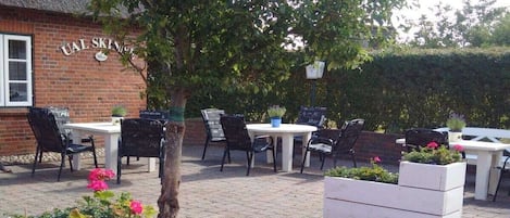 Un área de estar al aire libre con mesas y sillas, un edificio de ladrillo con un letrero y plantas en macetas.